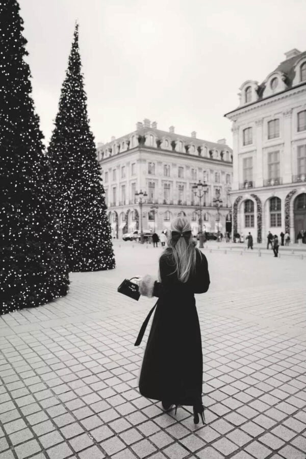 Emily wearing long winter coat with buildings in Paris in front