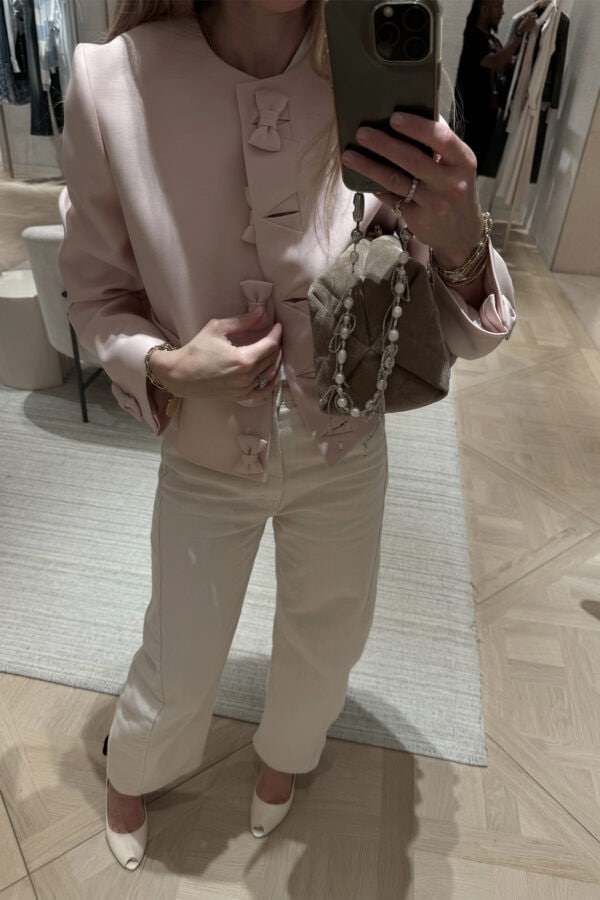 Emily wearing pink button jacket with bows and cream jeans