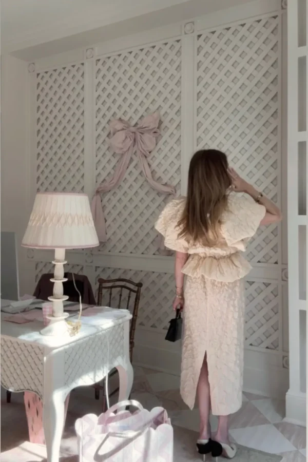 Emily wearing Ulla Johnson puff sleeve lace peplum skirt and top set in office with pink bow and decor