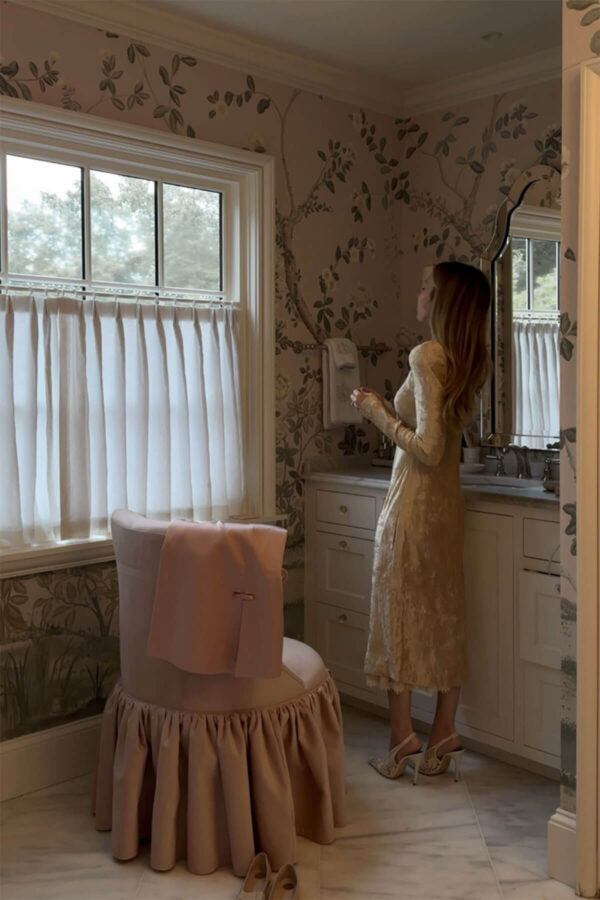 Emily wearing dress getting ready with vanity chair and floral wallpaper for bathroom